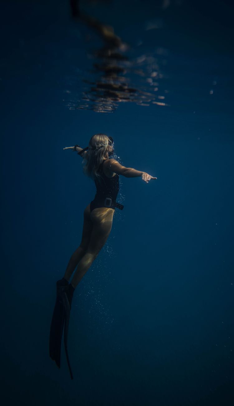 A woman gracefully dives underwater, exploring the serene ocean depths.